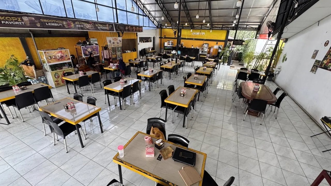 Ruang dalam Jaikopi di siang hari dengan meja kuning dan kursi hitam yang lega